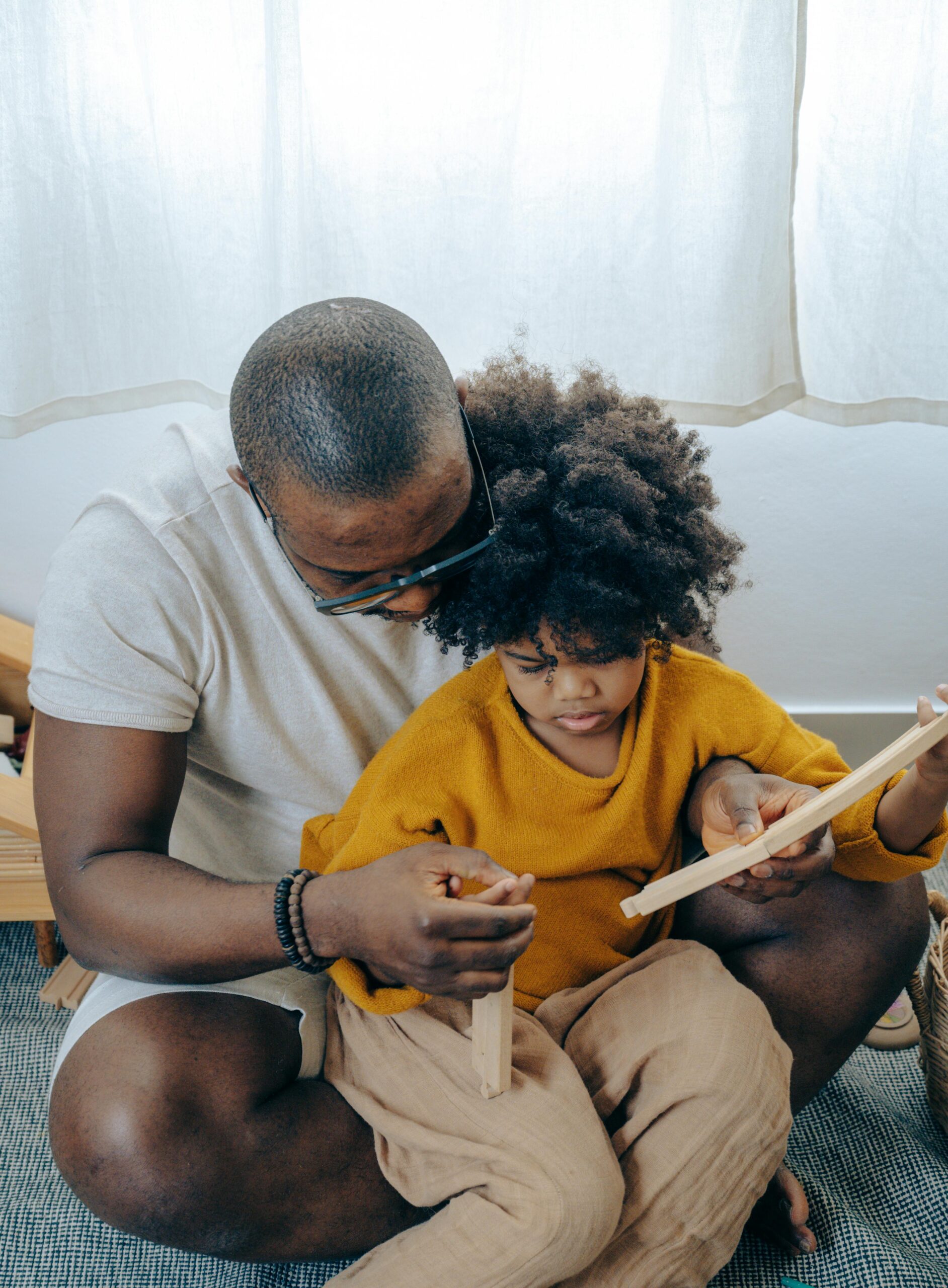 High angle of young black man taking care of little daughter while playing together sitting on floor